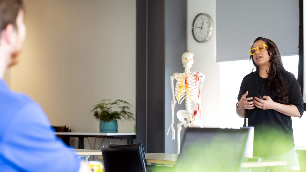 person standing and talking in a room with medical human skeleton in background